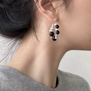 Detail of beaded hoop earrings with black and silver textured beads worn by a model