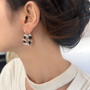 Detail of irregular silver beads and black stone hoop earrings on model for elegant style