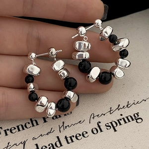 Detailed close-up of irregular silver beads and smooth black stone hoop earrings