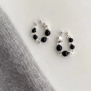Detail view of irregular silver beads and polished black stones on elegant hoop earrings