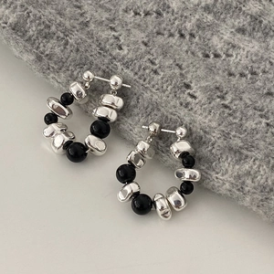 Detail of silver beaded hoop earrings with irregular metal charms and black beads