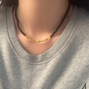 Detail of beaded black stone necklace with golden cube accents on a grey sweater