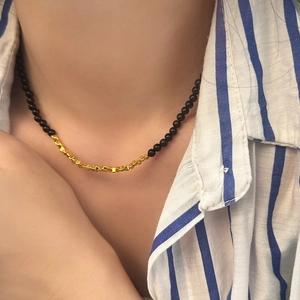 Detail of beaded necklace with black round stones and polished gold cube accents