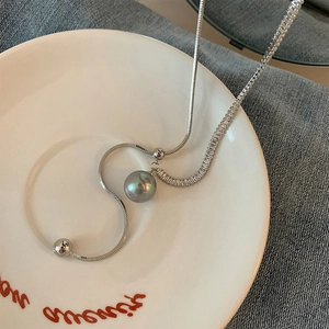 Long silver snake chain necklace with pearl pendant and metal beads on a white ceramic dish