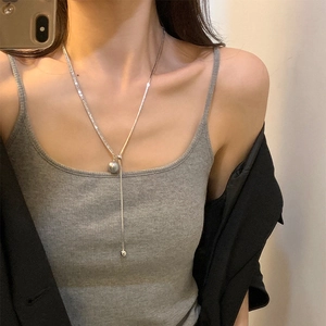 Detailed close-up of a silver long chain necklace with gray pearl and tassel on neck