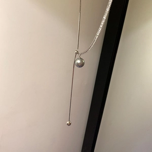 Detailed close-up of a silver Y-necklace with a grey pearl and round metal pendant