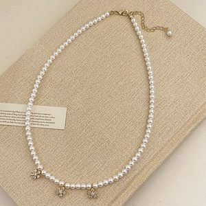 Gros plan d'un collier de perles avec pendentifs fleurs dorées sur support texturé