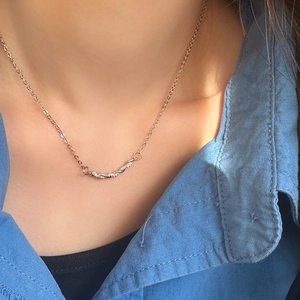 Gros plan du pendentif barre torsadée avec zircons sur une chaîne argentée portée par un mannequin