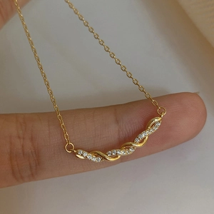 Collier élégant doré avec pendentif torsadé en zircone présenté sur un doigt
