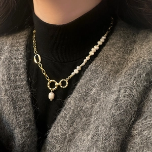 Detail of elegant gold chain and pearl necklace worn over a black turtleneck and grey knit
