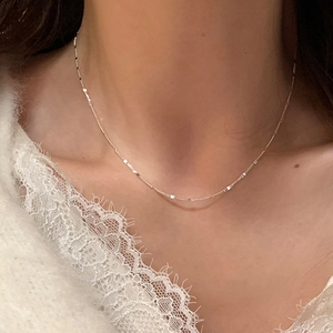 Close-up of a delicate silver minimalist necklace with shimmering square sequins on a model