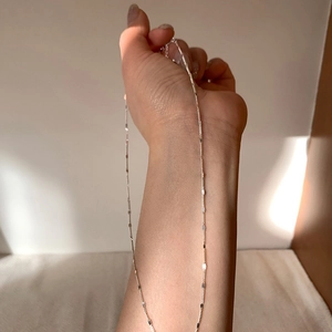 Detail view of a minimalist silver dainty chain necklace worn on the arm