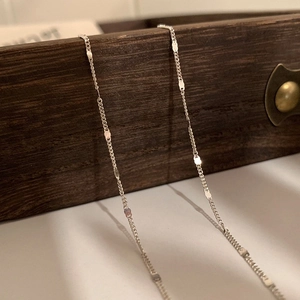 Minimalist silver chain necklace with polished oval links draped over a dark wood box