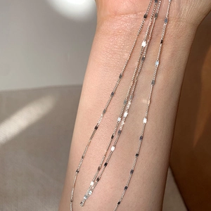 Close-up of minimalist silver chain necklaces cascading elegantly over a model's arm