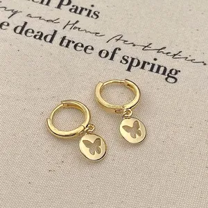 Elegant gold butterfly hollow hoop earrings with pendant on beige linen background