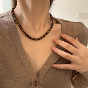 Gros plan du collier en perles d'oeil de tigre sur un cardigan marron montrant la texture