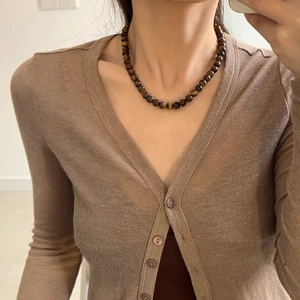 Gros plan d'un collier en perles d'œil de tigre vintage porté sur un gilet en maille