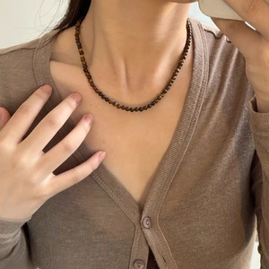 Gros plan d'un collier en pierre d'oeil de tigre style Maillard sur un pull marron