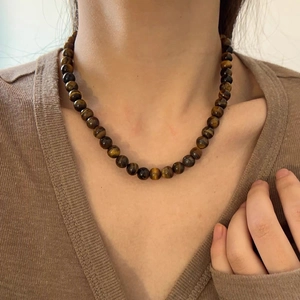 Gros plan du collier en œil de tigre naturel porté avec un pull en maille marron à col en V