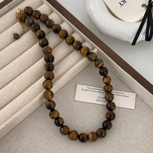 Détail d'un collier de perles en œil de tigre avec fermoir doré sur écrin à bijoux beige