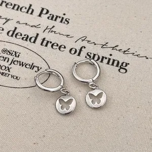 Detailed close-up of silver hollow butterfly round pendant earrings on linen fabric