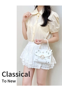 Detail view of floral embroidery and pearl handle on a white elegant handbag