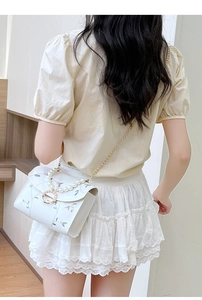 Detail of white square bag with floral embroidery, pearl handle, and golden chain strap