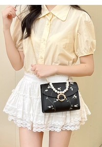 Detail of floral embroidery and pearl handle on a black mini flap crossbody bag