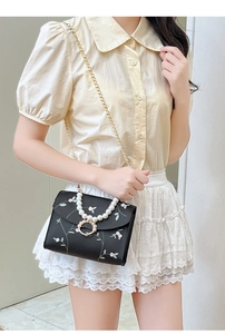 Detail of floral embroidery and pearl handle on a black crossbody bag with gold chain