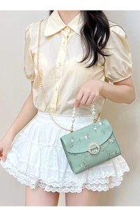 Detail of floral embroidery and pearl clasp on mint green crossbody bag shown on model