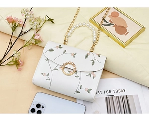 Detail of floral embroidery and pearl handle on a white faux leather crossbody bag