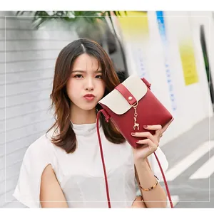 Detail of color-block crossbody bag with deer pendant shown on a street backdrop