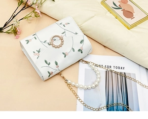 Detail of floral embroidery, pearl handle, and golden ring closure on a white handbag