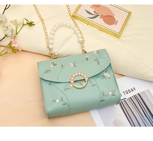 Detailed view of floral embroidery and pearl handle on light green crossbody bag