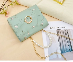 Detail of floral embroidery and pearl magnetic buckle on mint green crossbody bag