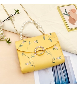 Close-up of yellow embroidered square bag with floral patterns and pearl top handle