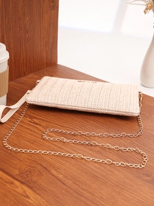 Detail of woven beige straw envelope bag featuring a gold chain strap on a wooden table