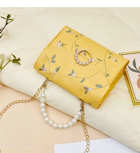 Detail of yellow floral embroidery and elegant pearl handle on a small square bag