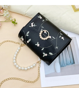 Detail of floral embroidery and elegant pearl clasp on black leather flap bag