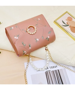 Close-up of floral embroidery and pearl-encrusted ring clasp on a pink crossbody bag