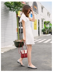 Mini red crossbody phone bag with gold deer charm worn by a model in a white dress