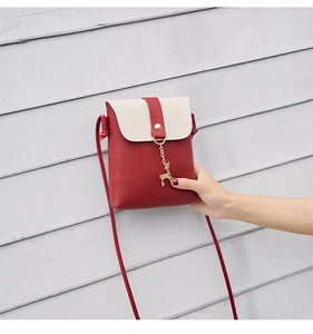 Detail shot of red and cream contrast crossbody bag with gold deer pendant decoration
