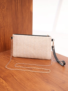 Detail of woven straw envelope bag featuring herringbone pattern and gold chain strap