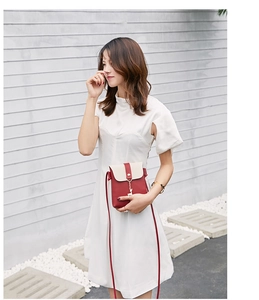 Detail of red and cream crossbody bag with a golden deer pendant on white dress