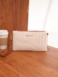 Detailed view of woven square bag with brown leather trim and golden metal logo