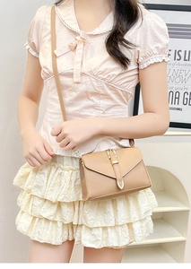 Close-up of a light brown leather crossbody bag featuring gold buckle and top handle