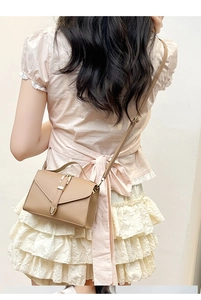 Detail of light brown leather crossbody bag with golden U-shaped buckle on a model