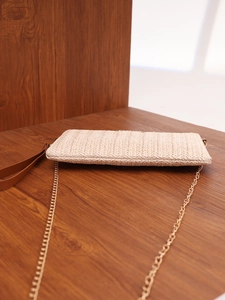 Close-up of woven straw handbag texture with gold chain and leather handle on wood