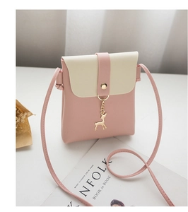 Detail shot of mini pink crossbody phone bag with gold deer charm on white table