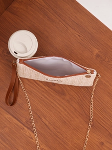 Detailed view of woven beige straw bag with gold chain strap and zipper on wooden desk